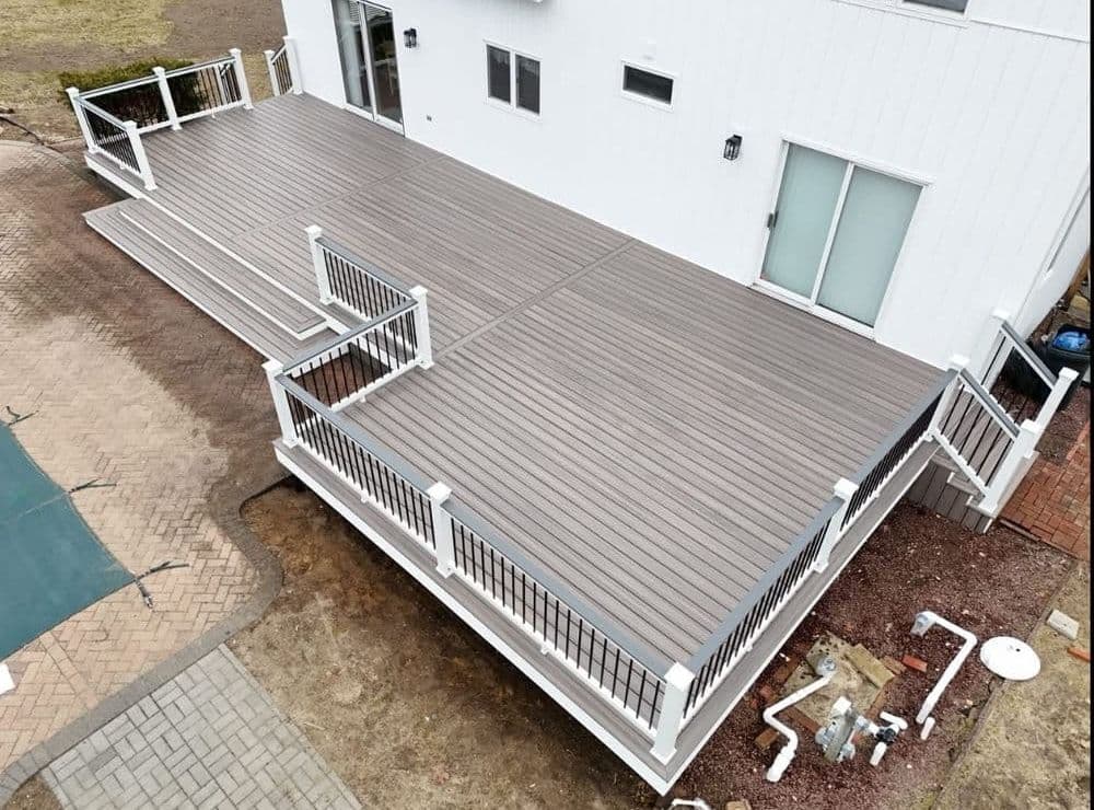 Aerial view of a large outdoor deck with railings, adjacent to a modern white house.