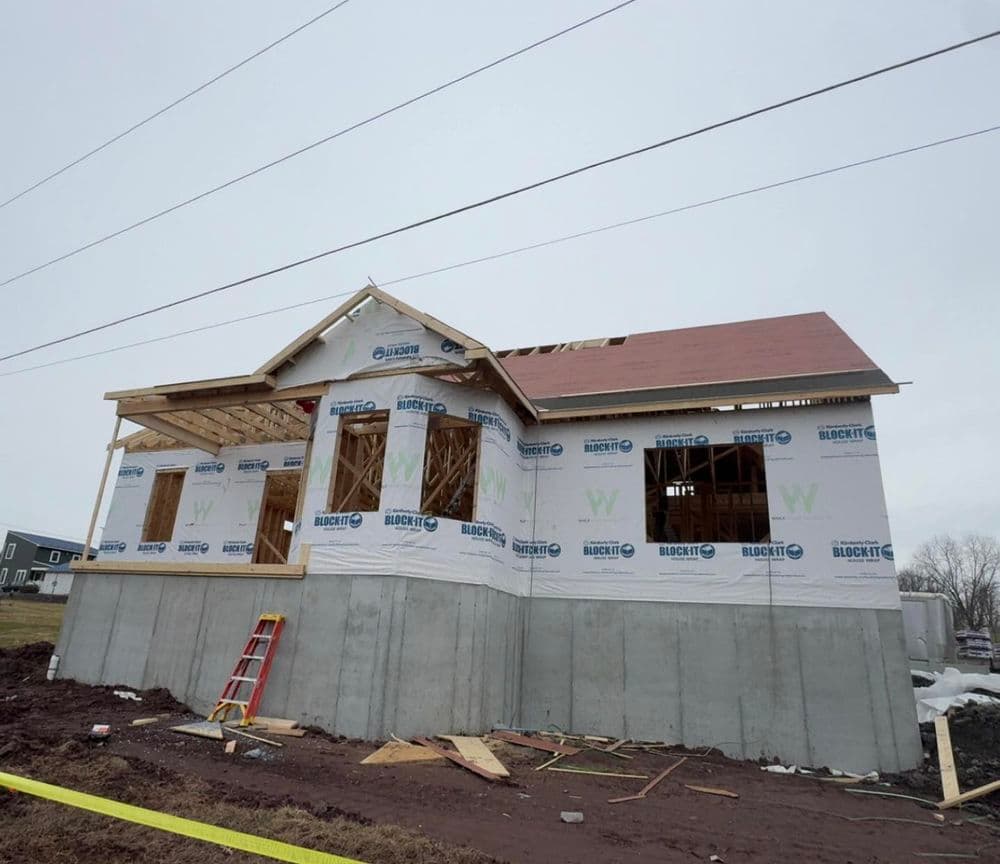 Newly constructed house with partial roof, covered in insulation and surrounded by construction materials.